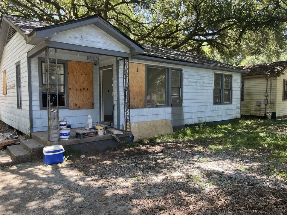 Small house before remodel, with boarded-up windows and worn siding