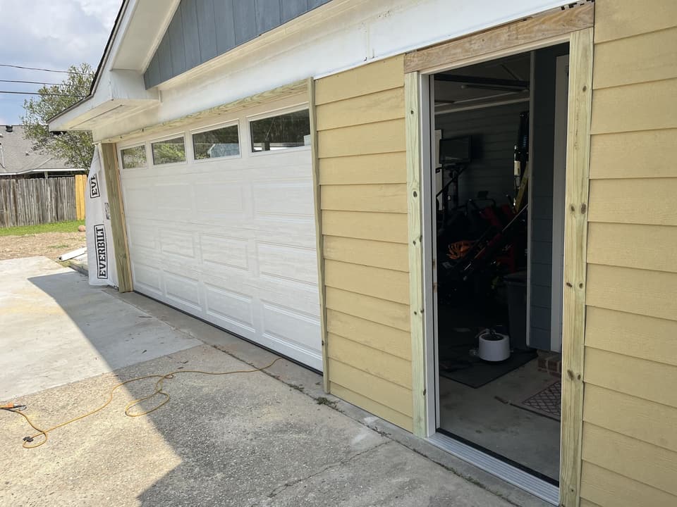 Garage being enclosed with yellow lap siding, a new garage door and a framed entry door