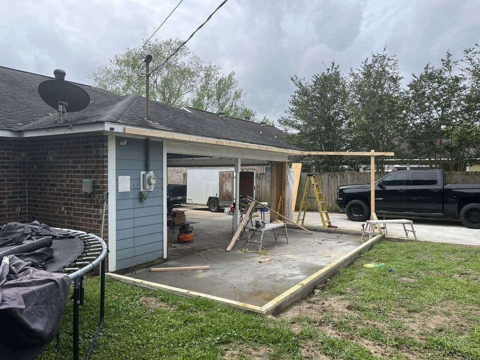 Concrete slab and posts at the back of a brick house, before the room addition