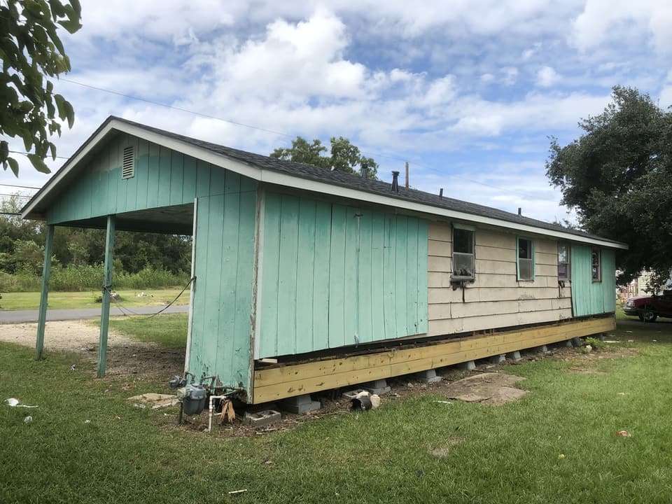 Raised house with worn green panel siding before replacement