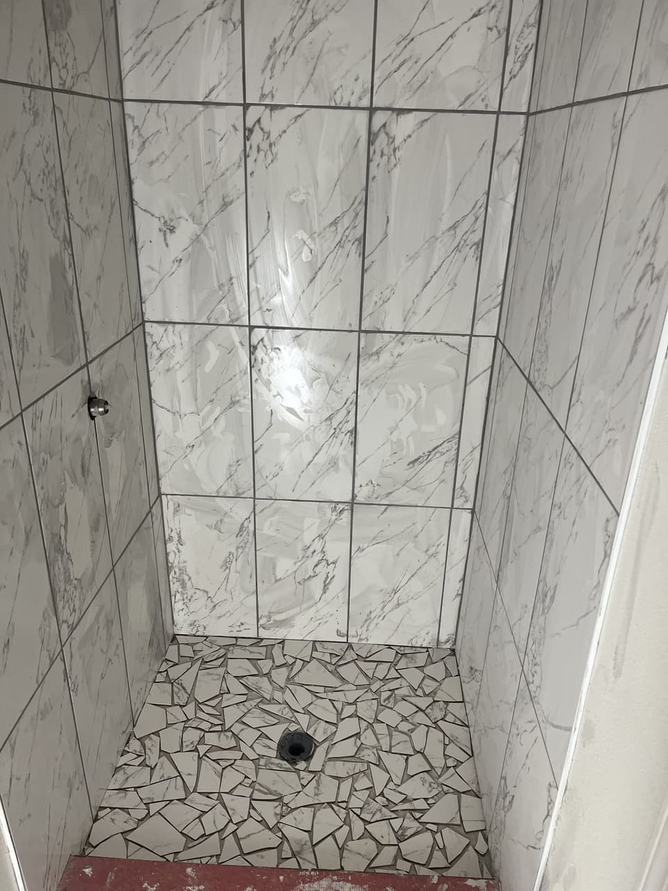 Finished walk-in shower with large marble-look wall tile and a mosaic floor